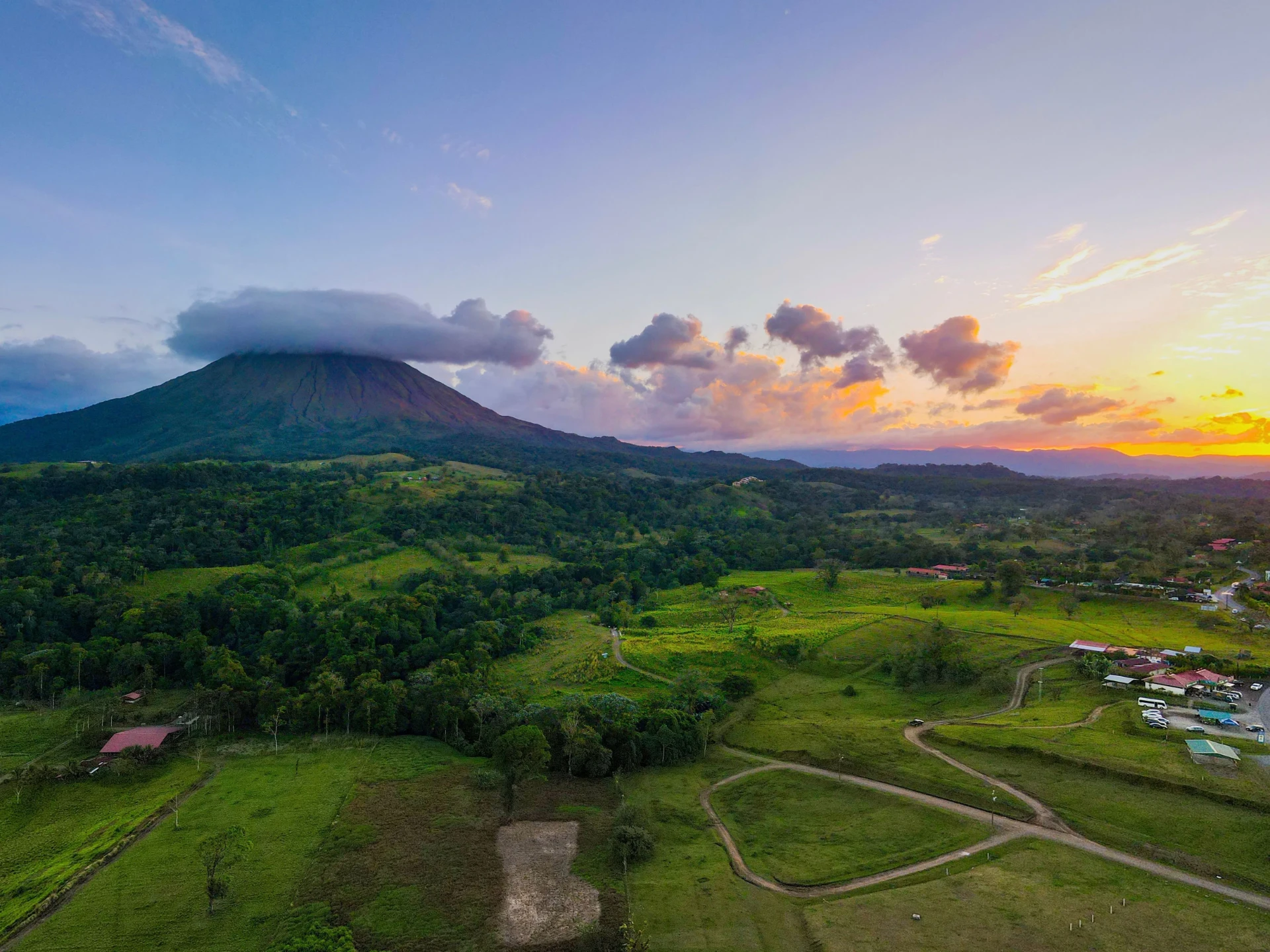 Rural farming community and fields at sunset beneath a volcano