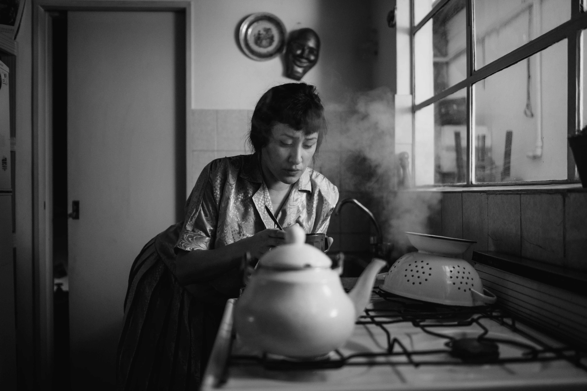 A woman preparing tea in a domestic kitchen, steam rising from the kettle