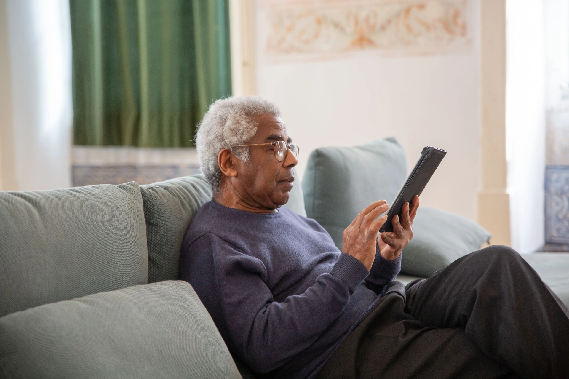 An older man using a tablet at home on a sofa