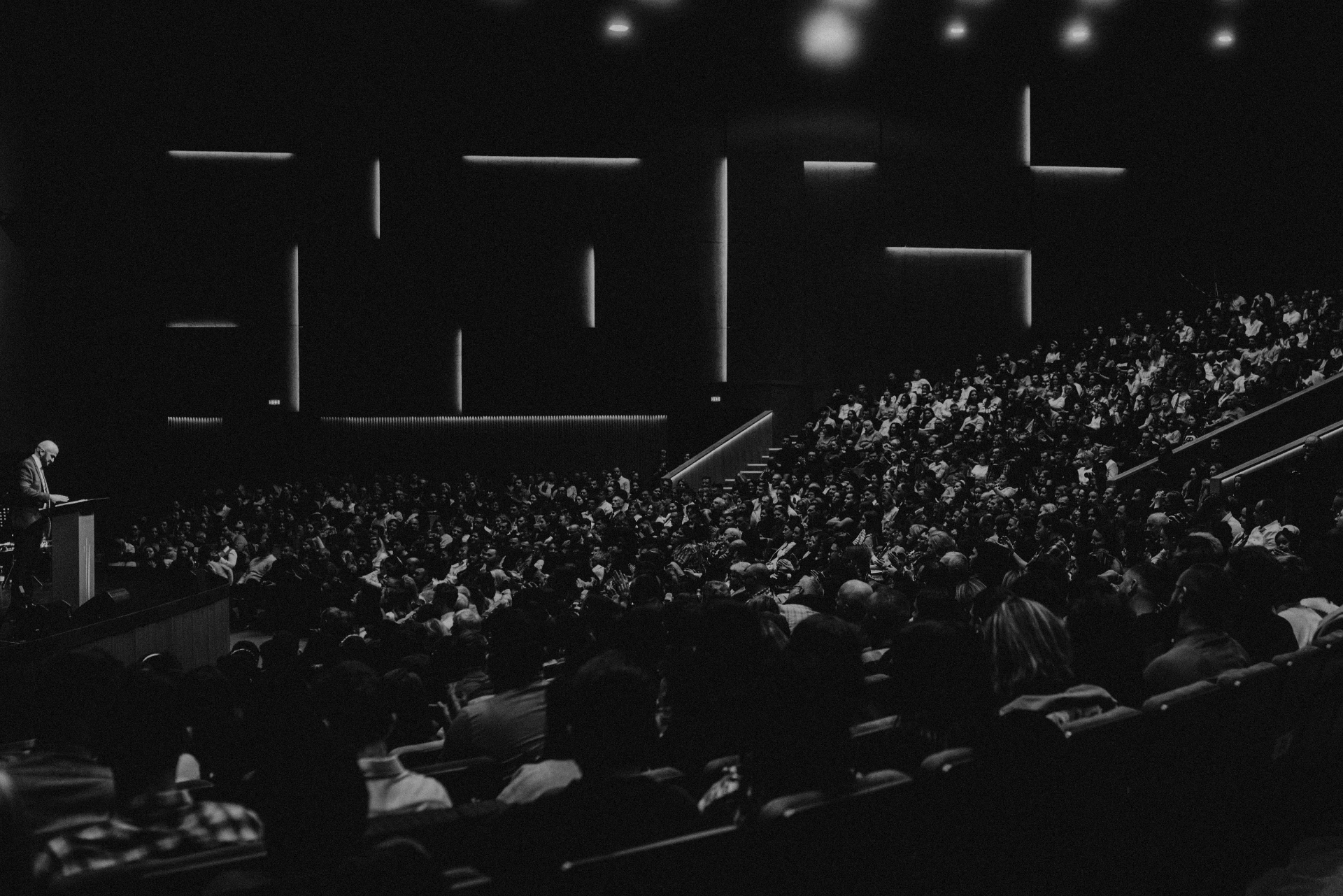 A speaker at a lectern addressing a large auditorium audience