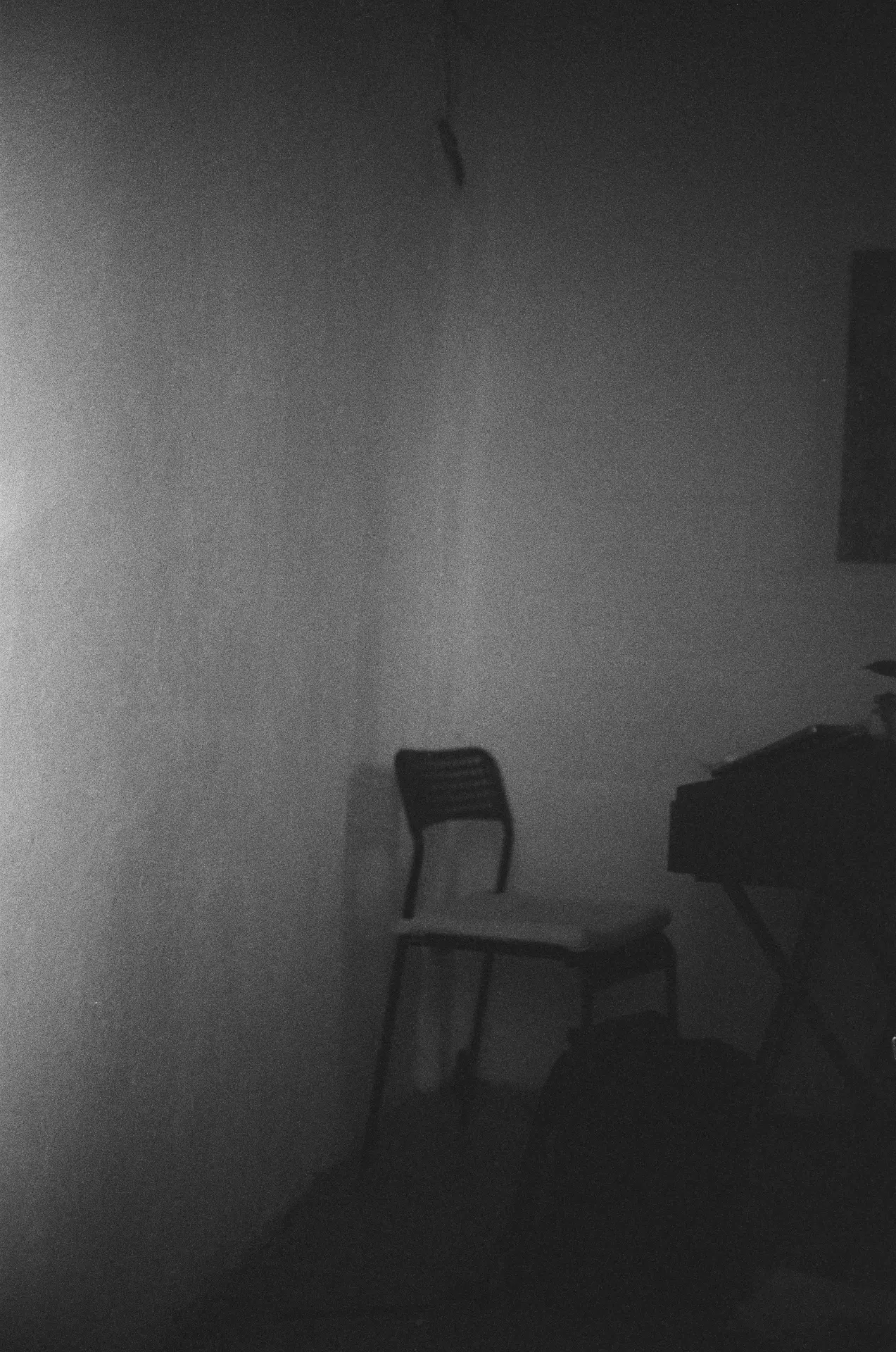 A grainy black-and-white photograph of a single chair in a dark, empty room